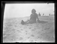 fo040094: Een kind, in bloemenjurk, zittend op het strand